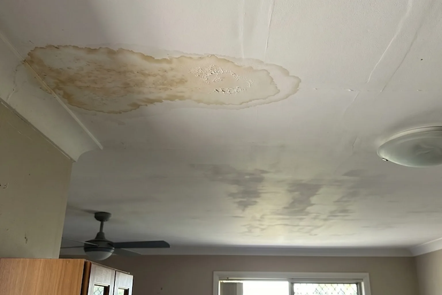 A brown water stain spreading across a ceiling below a roof leak